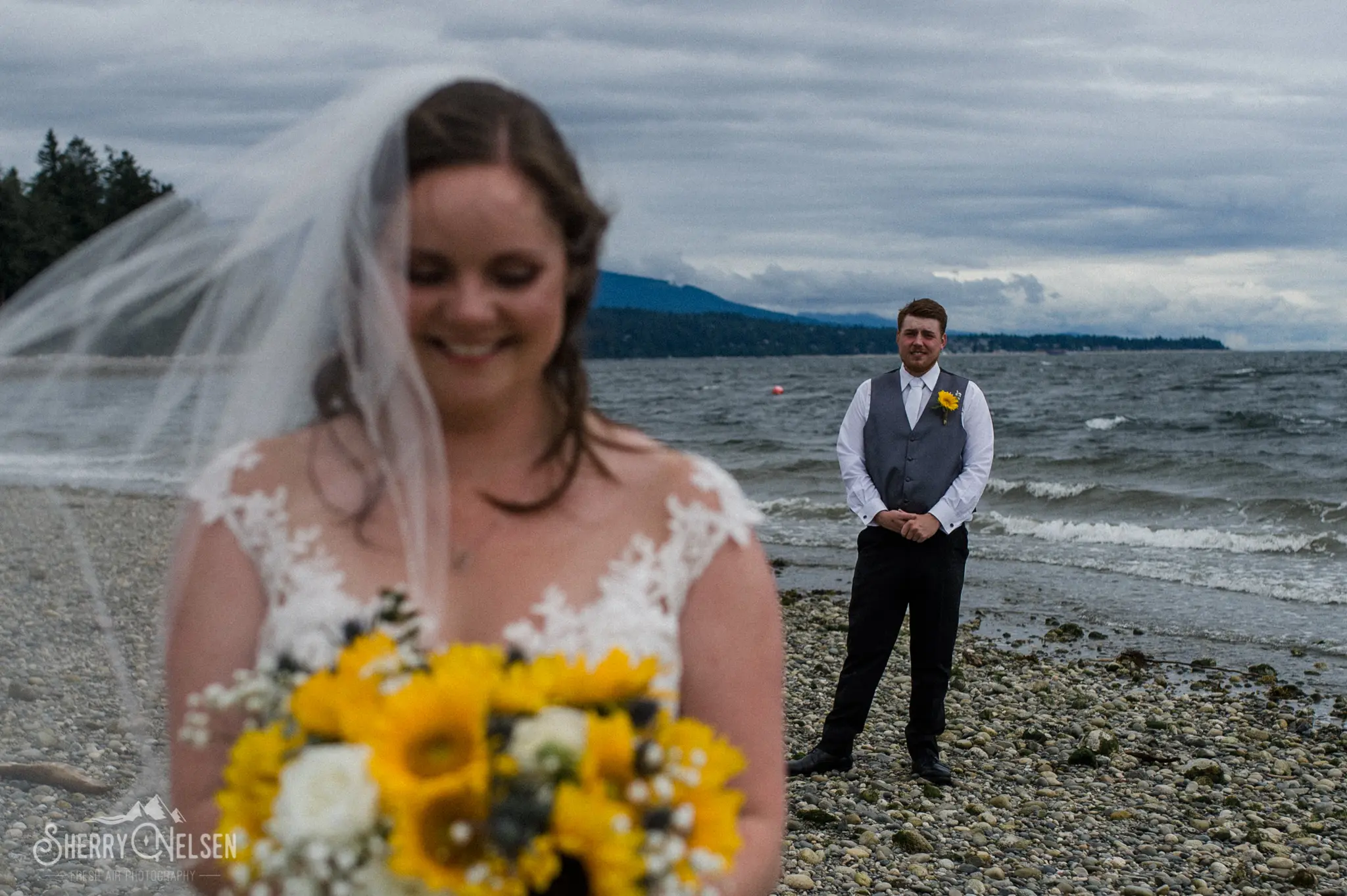 groom stands behind his bride as she smiles at her gorgeous bouquet by Coastal Wedding Events