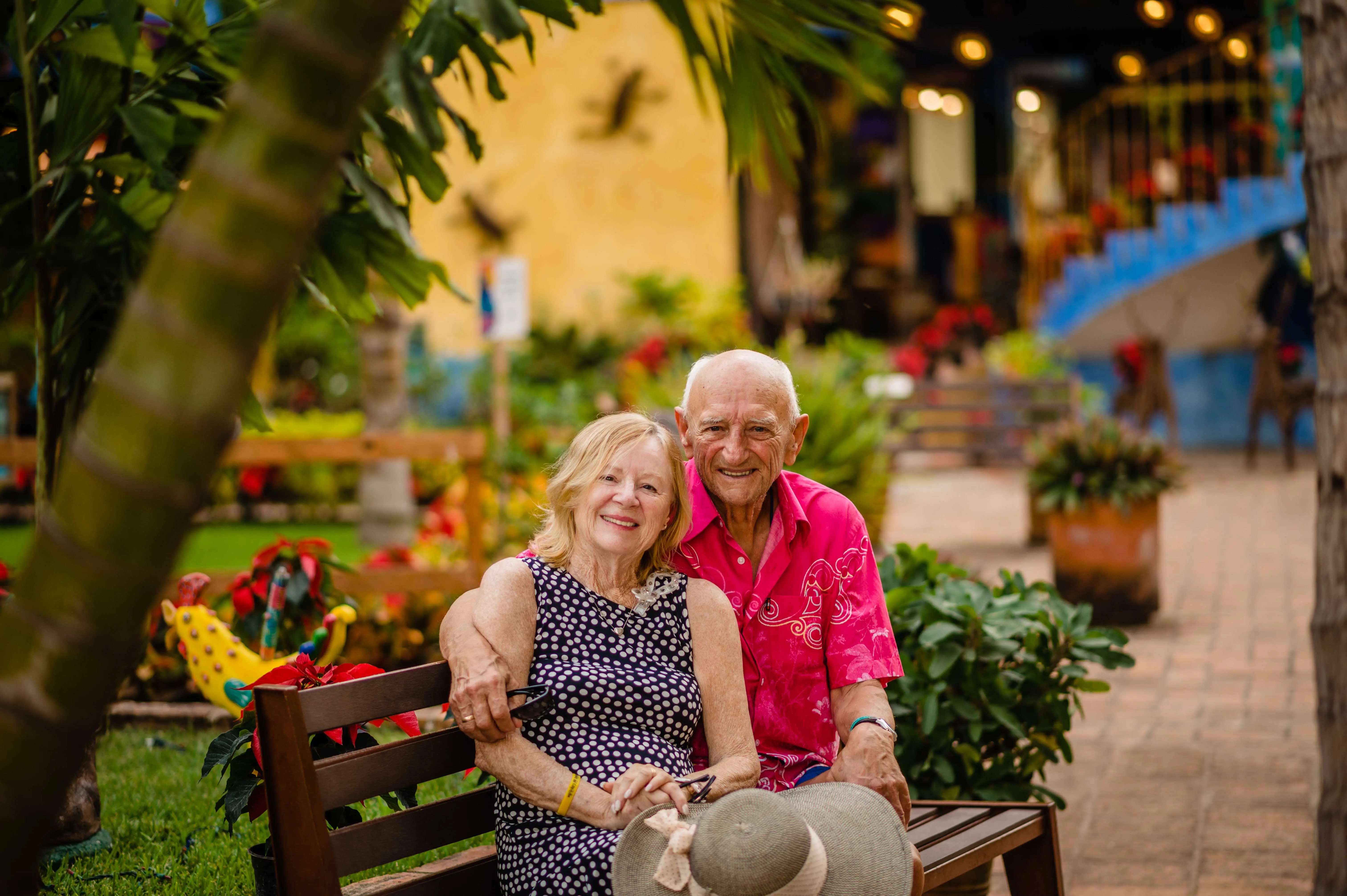 a couple who has been married for 59 years sits on a park bench in Mexico and smiles for the camera.