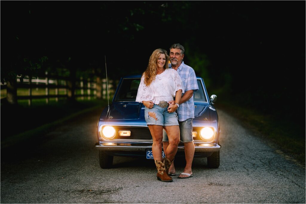 sunshine coast bc photographer sherry nelsen of fresh air photography stands smiling with her husband in front of a classic car