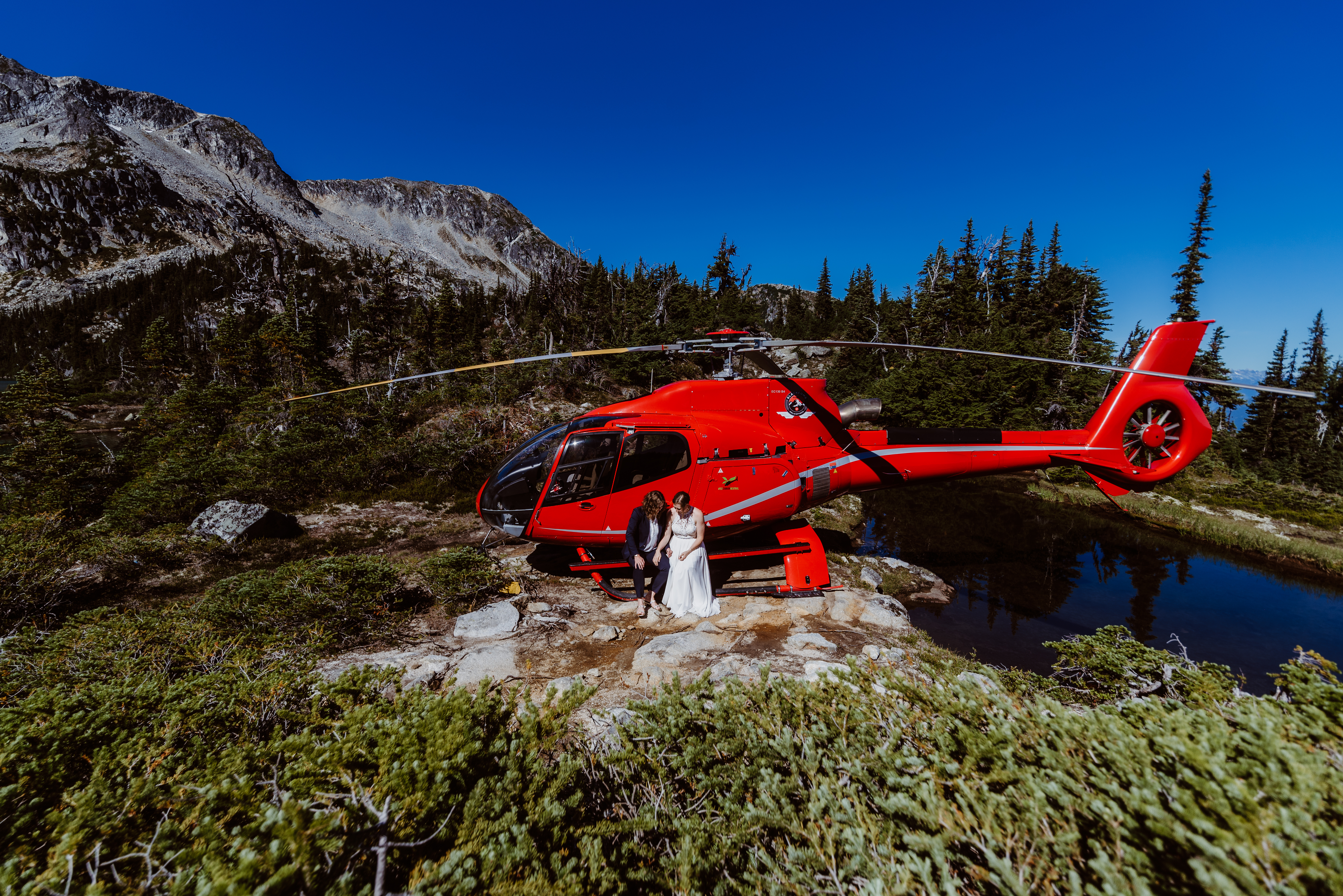 a bride and groom stand in front of a red helicopter during theiir sunshine coast bc wedding with photographer sherry nelsen 